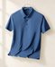 Haze blue polo shirt on a hanger against an ivory wall.