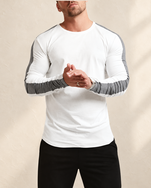 White long-sleeve T-shirt with charcoal sleeve stripes, worn against an ivory wall.
