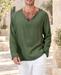Olive green long-sleeve V-neck shirt worn with white trousers in a pale stone courtyard.