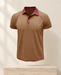 Brown short-sleeve polo with burgundy collar and contrast stitching against an ivory gallery wall.