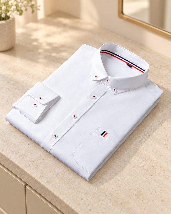 Folded white dress shirt with red-thread buttons and tricolor trim on a pale stone console.