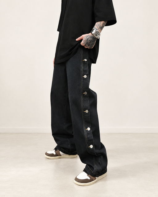 Loose black jeans with six visible silver side buttons in an ivory interior.