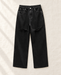 Black loose straight-leg jeans with distressed knees, laid on ivory linen.