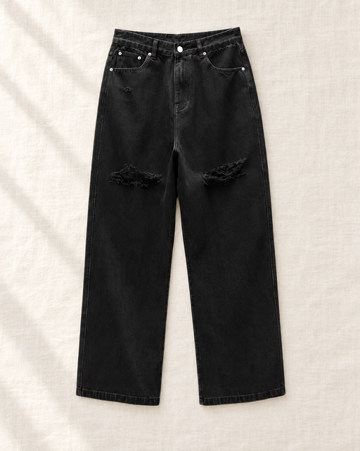 Black loose straight-leg jeans with distressed knees, laid on ivory linen.