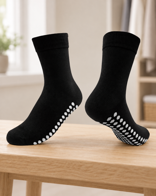 Pair of black socks with white oval sole grips displayed on a pale wooden bench.