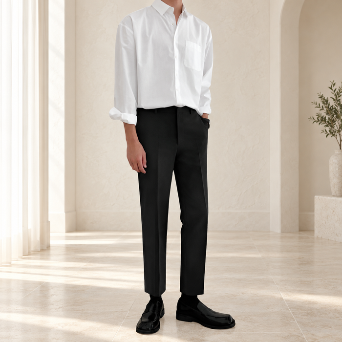 Black straight-leg trousers worn with a white shirt against a softly lit ivory interior.