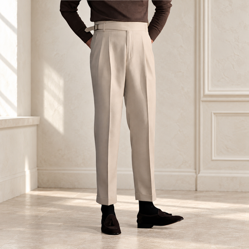 Beige high-waisted pleated trousers with a side adjuster, worn with a brown sweater in an ivory room.