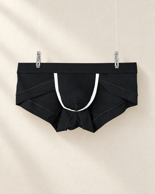 Black briefs with white trim hanging from two clips against an ivory display wall.