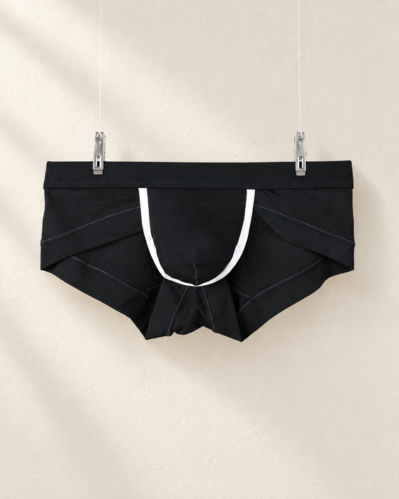Black briefs with white trim hanging from two clips against an ivory display wall.