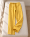 Mustard yellow drawstring pajama trousers laid on an ivory upholstered bench.