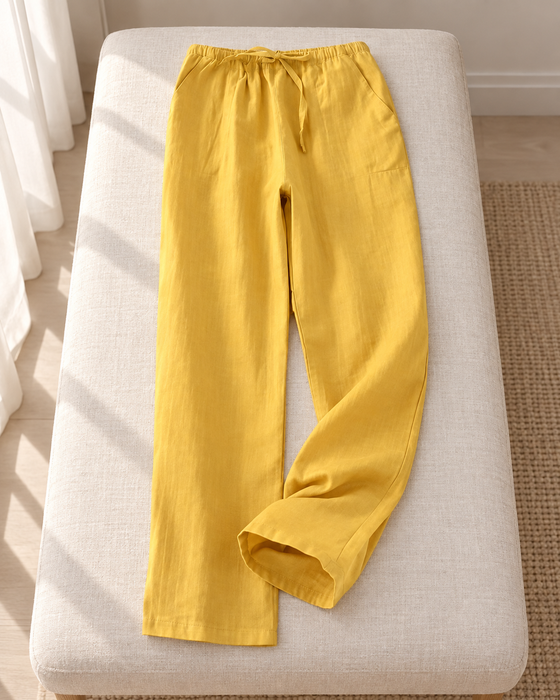 Mustard yellow drawstring pajama trousers laid on an ivory upholstered bench.