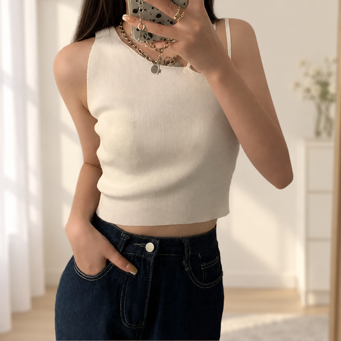 Cream asymmetrical ribbed sleeveless top worn with dark jeans in a light interior.