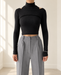 Black ribbed two-piece long-sleeve top with a high collar, worn with grey trousers in an ivory interior.