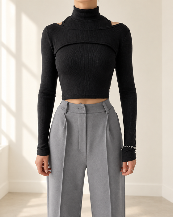 Black ribbed two-piece long-sleeve top with a high collar, worn with grey trousers in an ivory interior.
