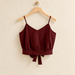Burgundy camisole with gathered waist and bow ties on a wooden hanger against an ivory wall.