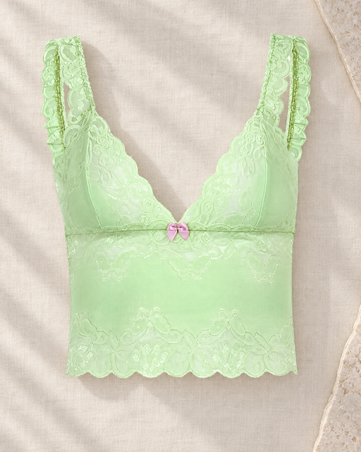 Pale green lace camisole with a pink bow laid on ivory linen.