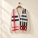 Beige knit cardigan with asymmetric black, white and red checks on a wooden hanger.
