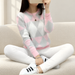 Pink and grey diamond-pattern sweater worn while seated on an ivory sofa