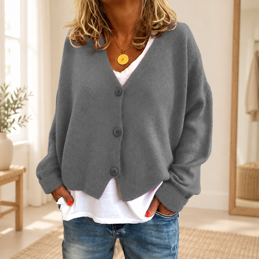 Grey V-neck cardigan with three buttons, worn over a white top and jeans in an ivory room.