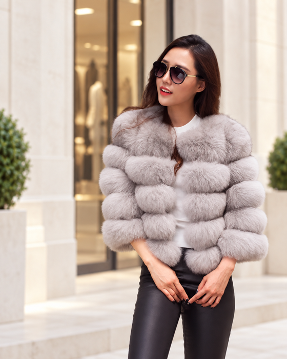 Light-grey textured short jacket with horizontal sections worn outside a pale stone boutique.