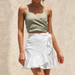 White wrap skirt with a side tie and ruffled hem, styled against pale stone.