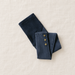 Folded blue jeans with three gold ankle buttons on ivory linen