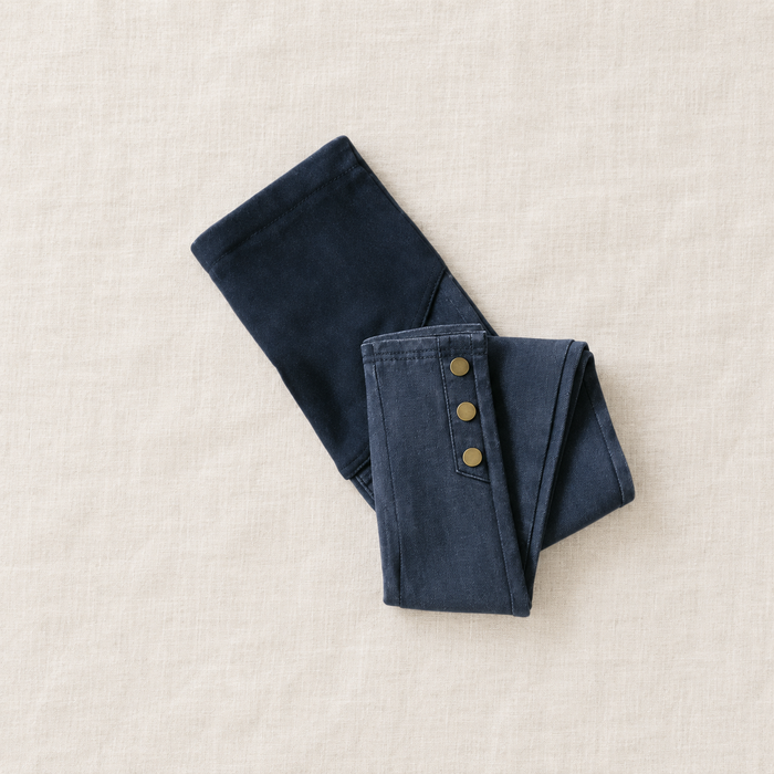 Folded blue jeans with three gold ankle buttons on ivory linen