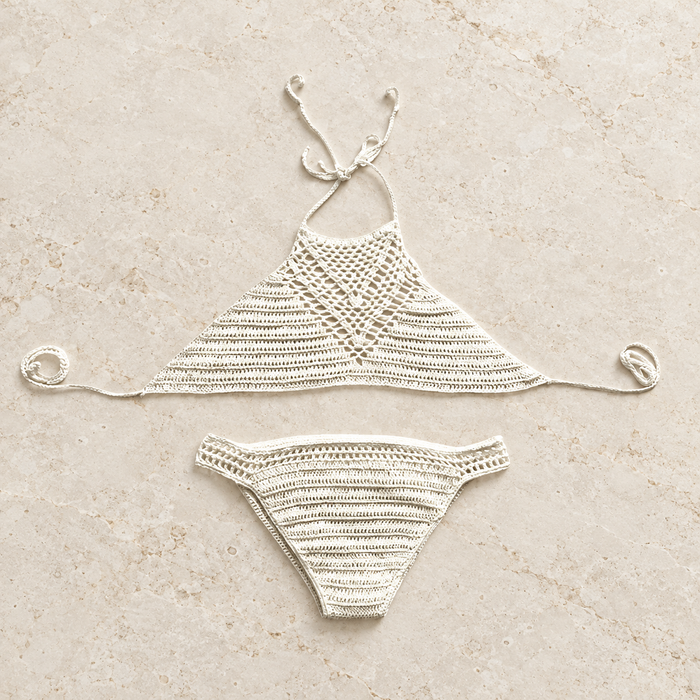 Ivory crochet two-piece swimwear arranged on a warm stone surface.