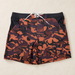 Orange and dark camouflage swim shorts on an ivory surface