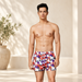 White beach shorts with a red and purple fruit print in a neutral resort setting.