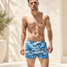 Blue beach shorts with an island and palm tree print in a neutral resort setting.