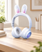 White headphones with pink bunny-ear inserts on a pale wooden desk in an ivory interior.