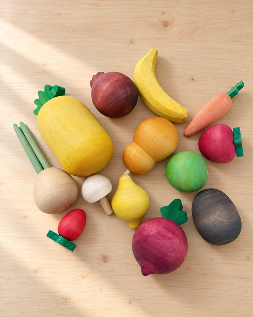 Thirteen colourful wooden fruit and vegetable toys arranged on a pale wooden table.