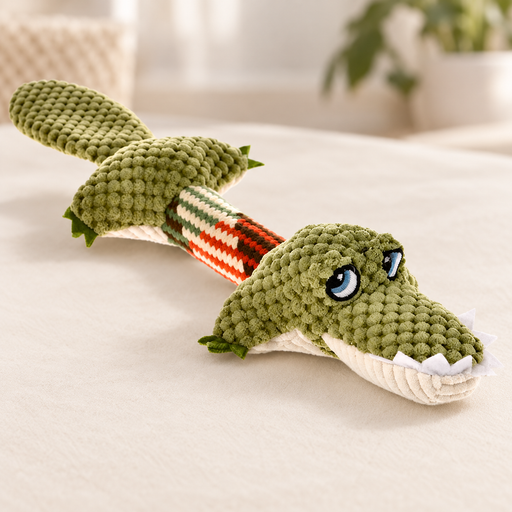 Olive crocodile dog toy with striped middle on a neutral surface.