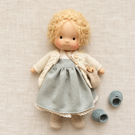 Blond cloth doll with grey dotted dress and knitted accessories on ivory linen
