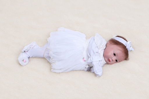 Vinyl doll lying sideways in a white dress with a bow headband and matching shoes