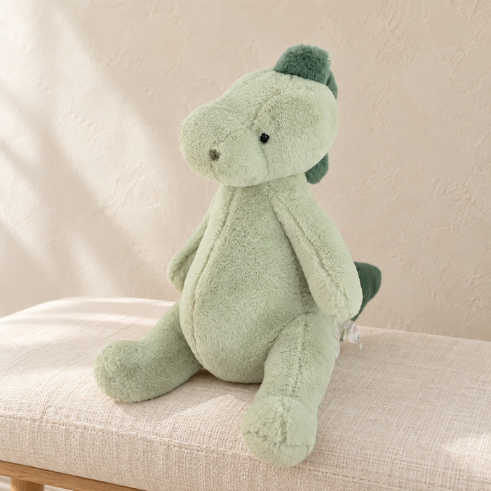 Sage green dinosaur plush on an ivory linen bench