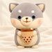 Grey Shiba plush holding a tan bubble-tea cup on ivory fabric.