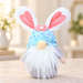 Blue sequinned bunny gnome with pink flower and white beard on a pale stone tabletop