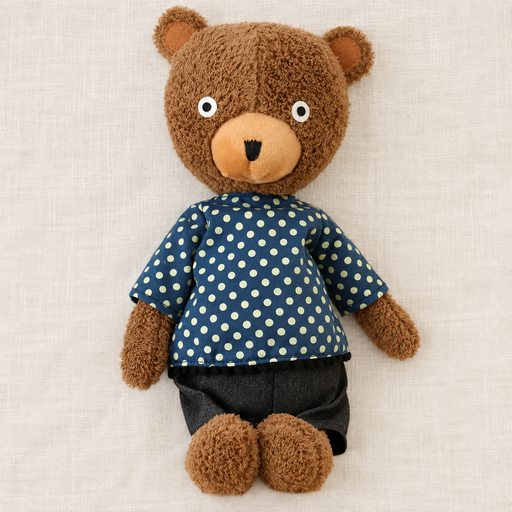 Brown teddy bear in a navy dotted shirt and dark shorts on ivory linen