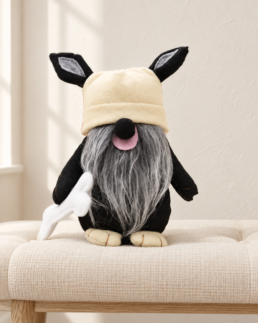 Black plush dog toy with a cream hat and grey beard on an ivory linen bench.