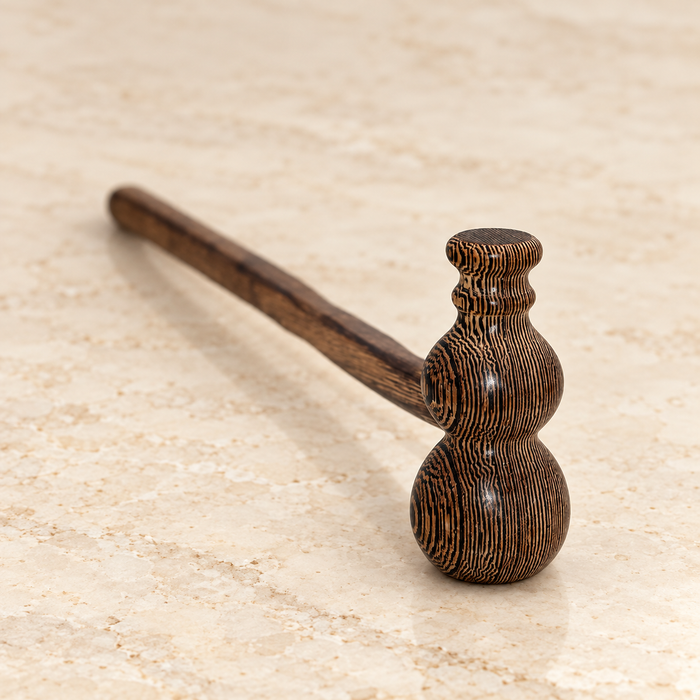 Dark striped wooden massage hammer resting on ivory stone