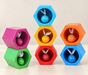 Seven colourful wooden bee cells and matching bees arranged on an ivory table.
