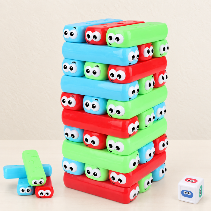 Colourful stacking block tower with cartoon eyes, loose blocks and a die on an ivory table.