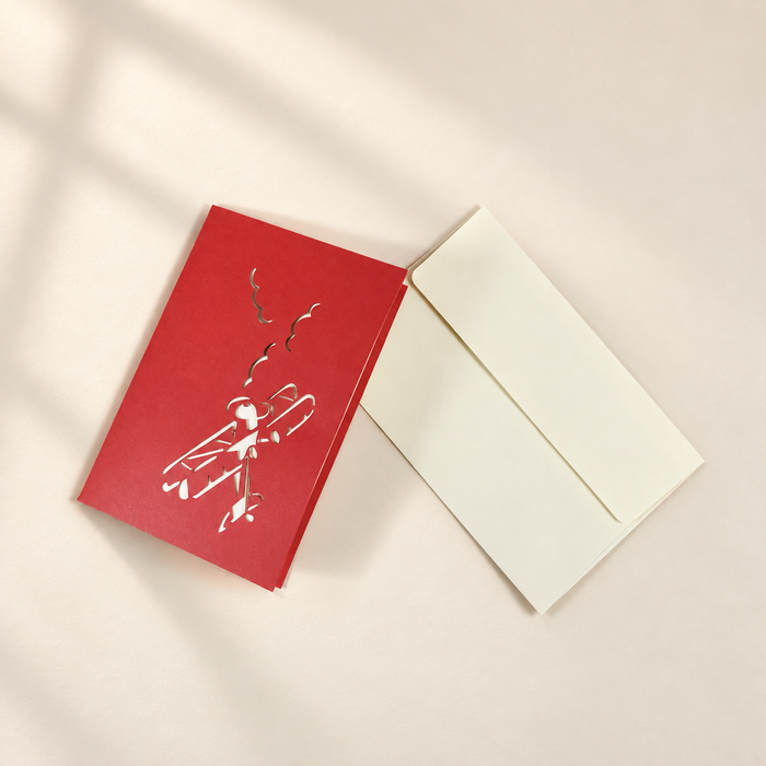 Closed red airplane greeting card beside a cream envelope