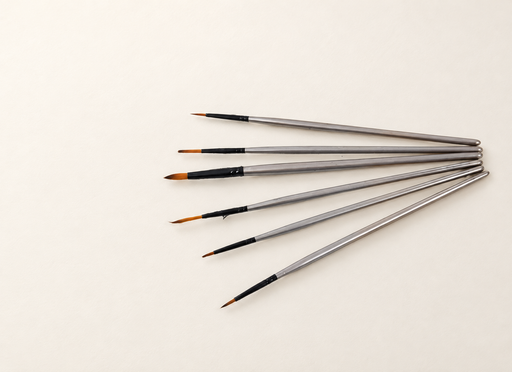 Six silver-handled paint brushes arranged in a fan on an ivory surface