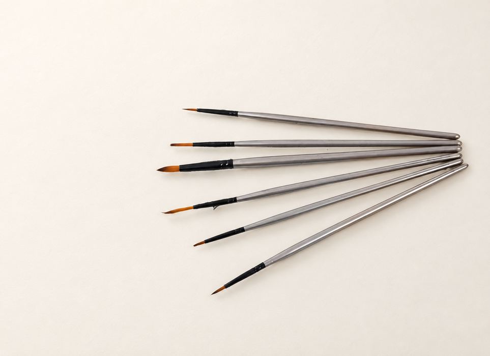 Six silver-handled paint brushes arranged in a fan on an ivory surface