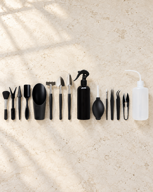 Black and white miniature gardening tools arranged on an ivory stone surface.