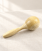 Natural wooden maraca resting diagonally on ivory linen.