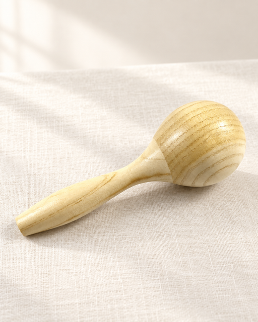Natural wooden maraca resting diagonally on ivory linen.